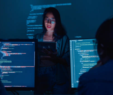 Женщина представляет код на нескольких экранах, помогая новичкам выбрать первый язык программирования.